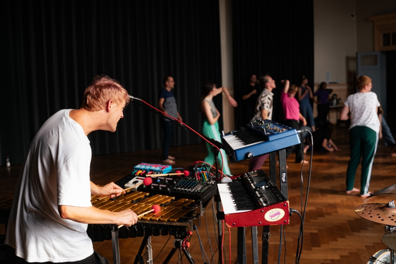Foto van een groep dansende mensen met muzikant met keyboard en microfoon op de voorgrond, beeld van deze Open Dance Jam