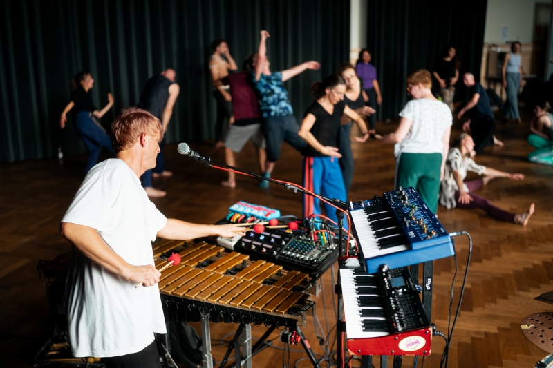 Foto van een groep dansende mensen met muzikant met keyboard op de voorgrond, beeld van deze Open Dance Jam